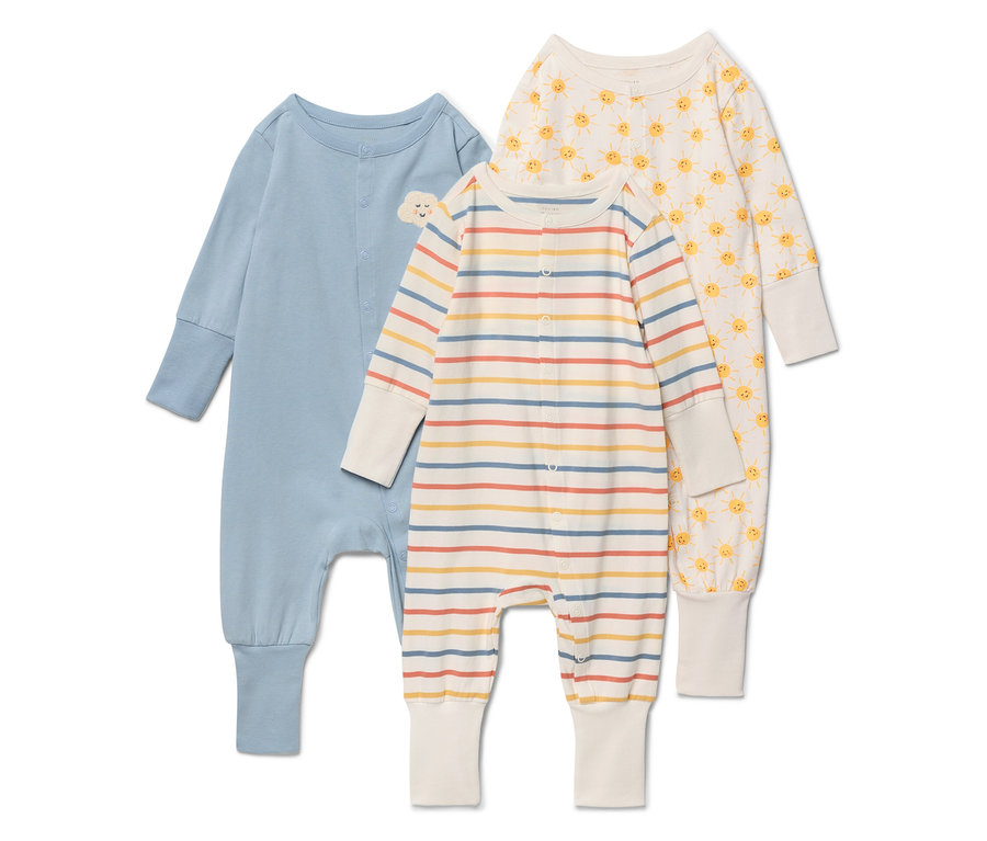 Trzy pajacyki niemowlęce leżą na białym tle. Lewy pajacyk jest niebieski z małym obłoczkiem na piersi. Środkowy pajacyk jest w paski w kolorach beżowym, żółtym, czerwonym i niebieskim. Prawy pajacyk jest kremowy we wzór żółtego słońca.