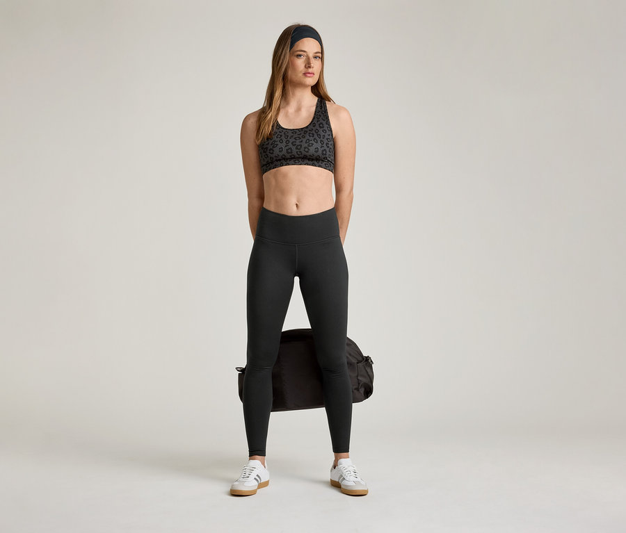 Kobieta w staniku sportowym i legginsach sportowych „ActiveSoft” z torbą sportową i tenisówkami.