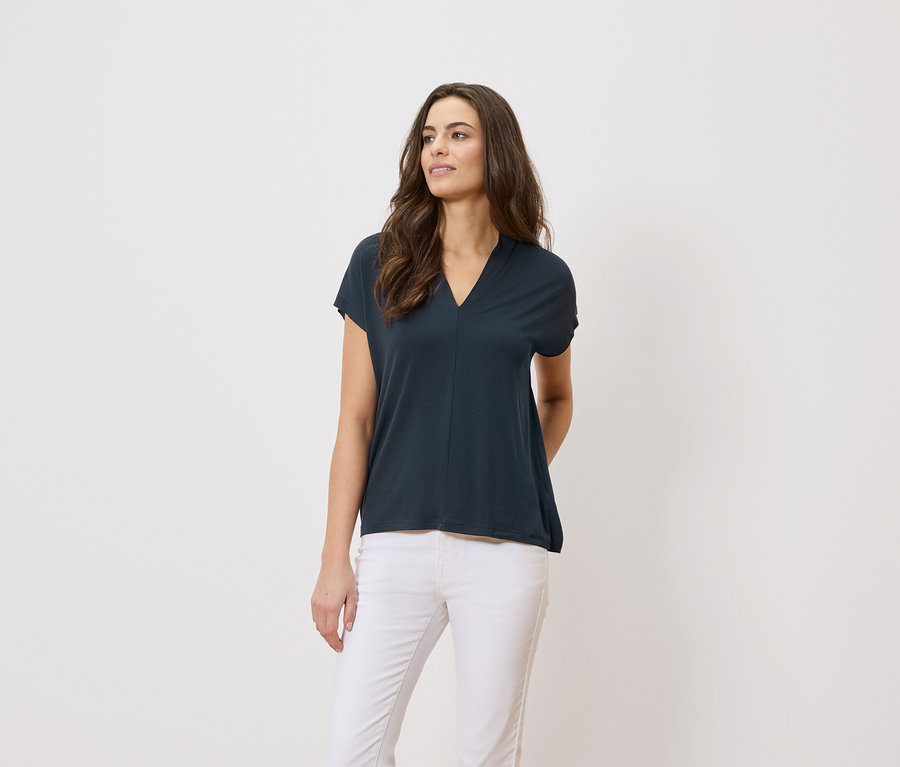 Kobieta ma na sobie granatową koszulkę i białe spodnie na białym tle.