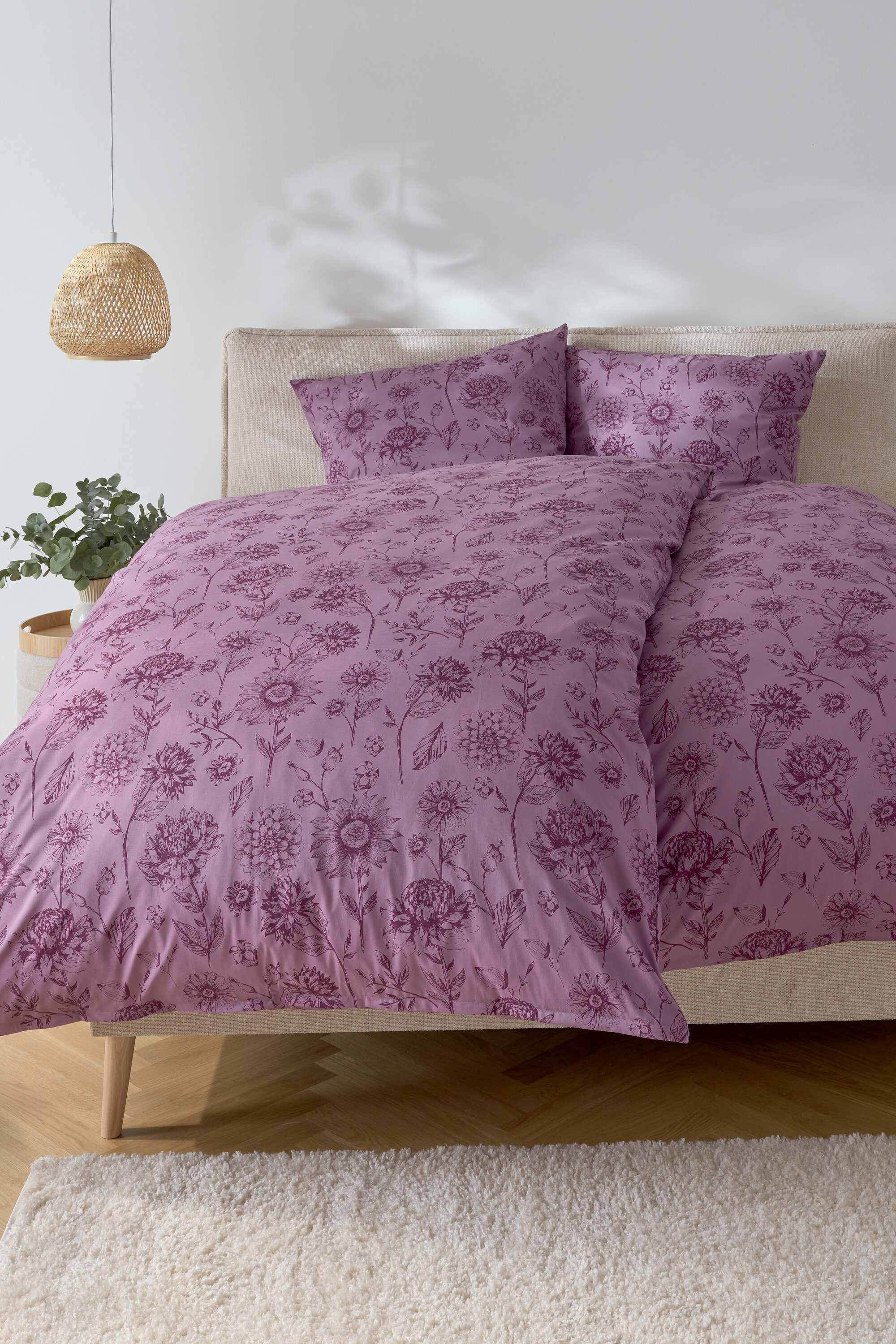 Sypialnia z łóżkiem z fioletową pościelą w kwiaty i dwiema poduszkami.