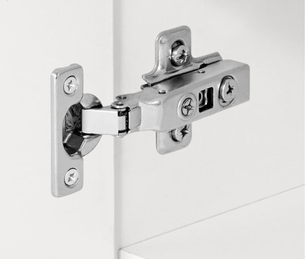 Szczegół srebrnego zawiasu na białej szafce.