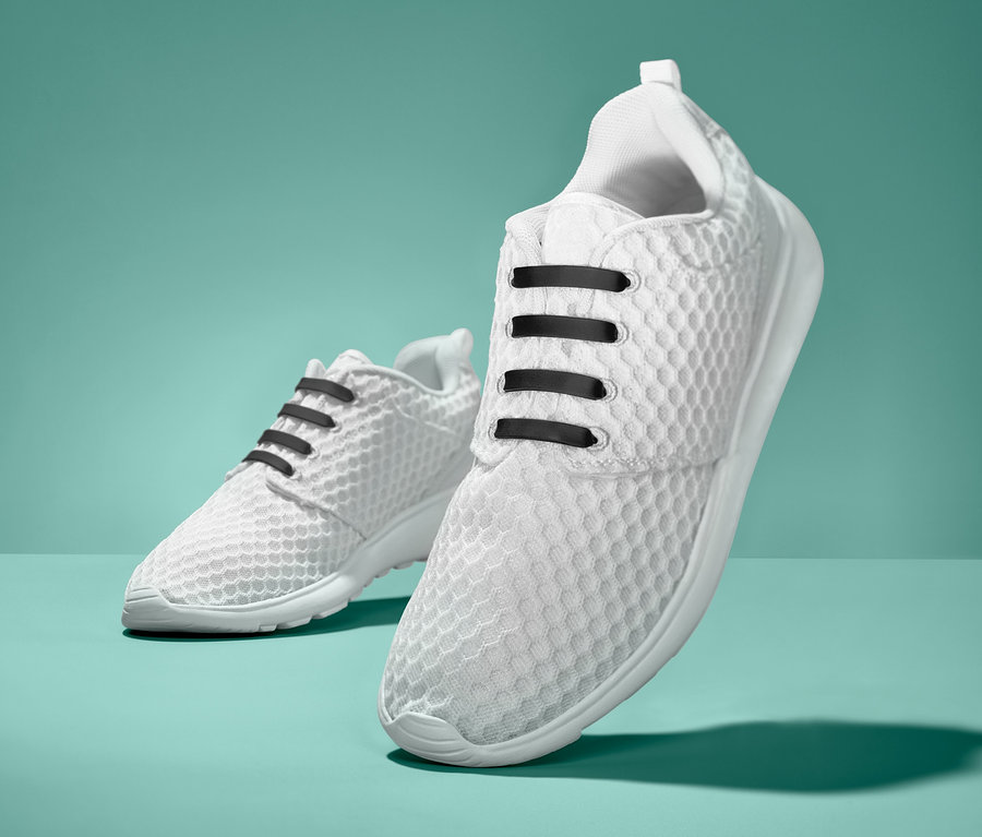 Dwa białe tenisówki z czarnymi elastycznymi sznurowadłami silikonowymi. Elastyczne sznurowadła silikonowe, 20 sztuk.