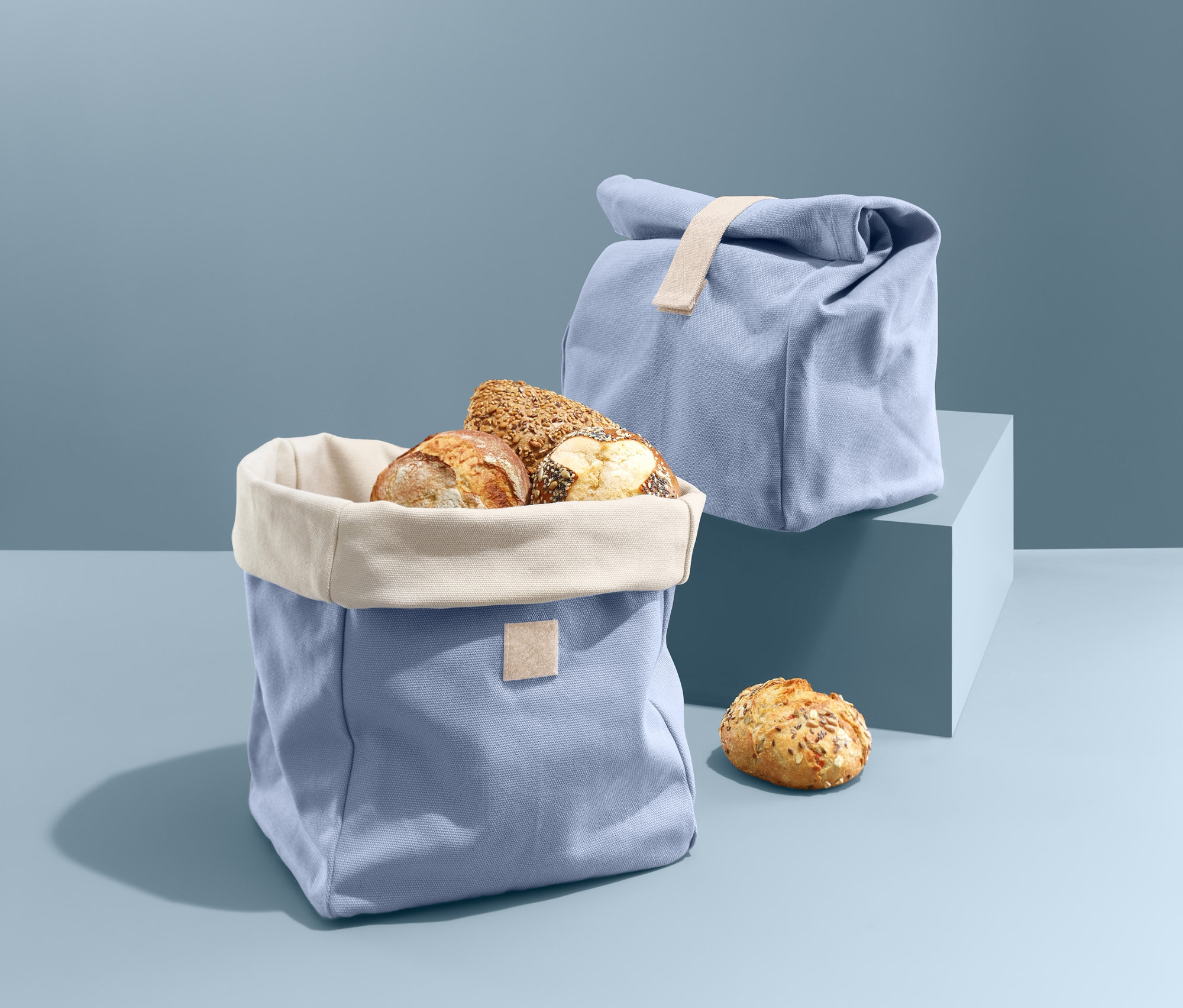Otwarta niebieska torba na pieczywo 2 w 1 wypełniona bochenkami chleba obok zamkniętej torby na pieczywo.