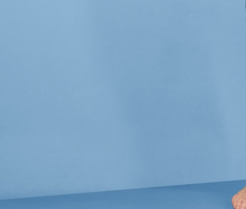 Uśmiechnięta kobieta pozuje w szarym podkoszulku i spodniach rekreacyjnych damskich z dżerseju na niebieskim tle.