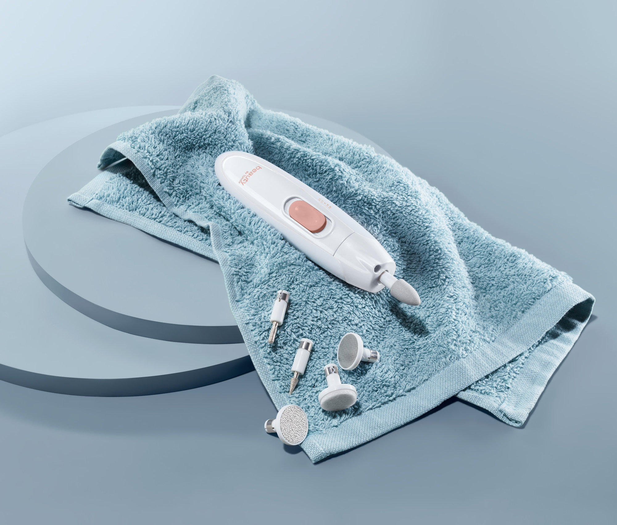 Urządzenie do manicure i pedicure leży na niebieskim ręczniku z nasadkami.