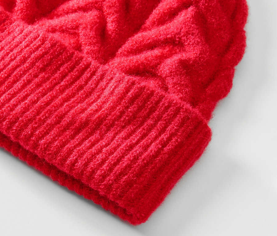 Zbliżenie na czerwoną czapkę z dzianiny z warkoczowym wzorem.