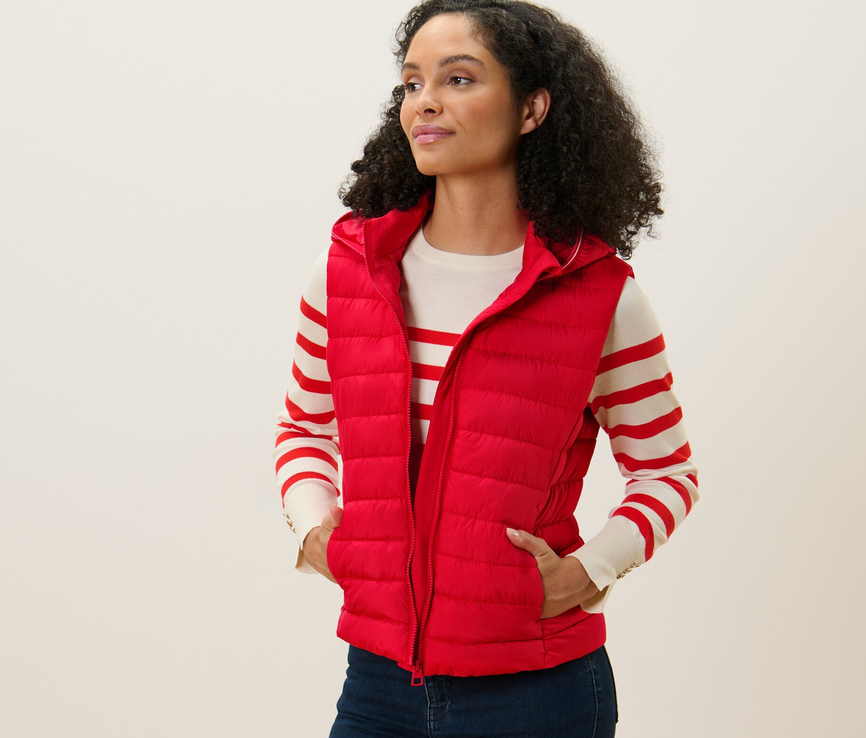 Kobieta ma na sobie kamizelkę pikowaną z kapturem w kolorze czerwonym, stoi i patrzy w lewo.