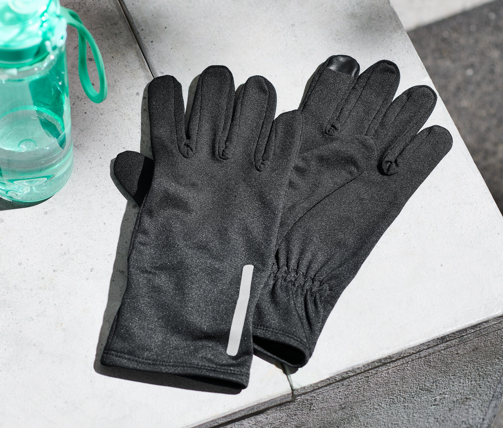 Na betonowej powierzchni leżą rękawiczki do biegania i butelka z wodą.