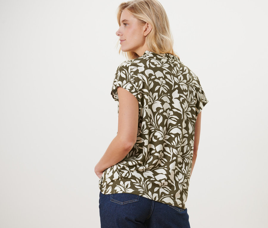 Kobieta stoi tyłem, ubrana w bluzkę z dekoltem w serek i dżinsy.