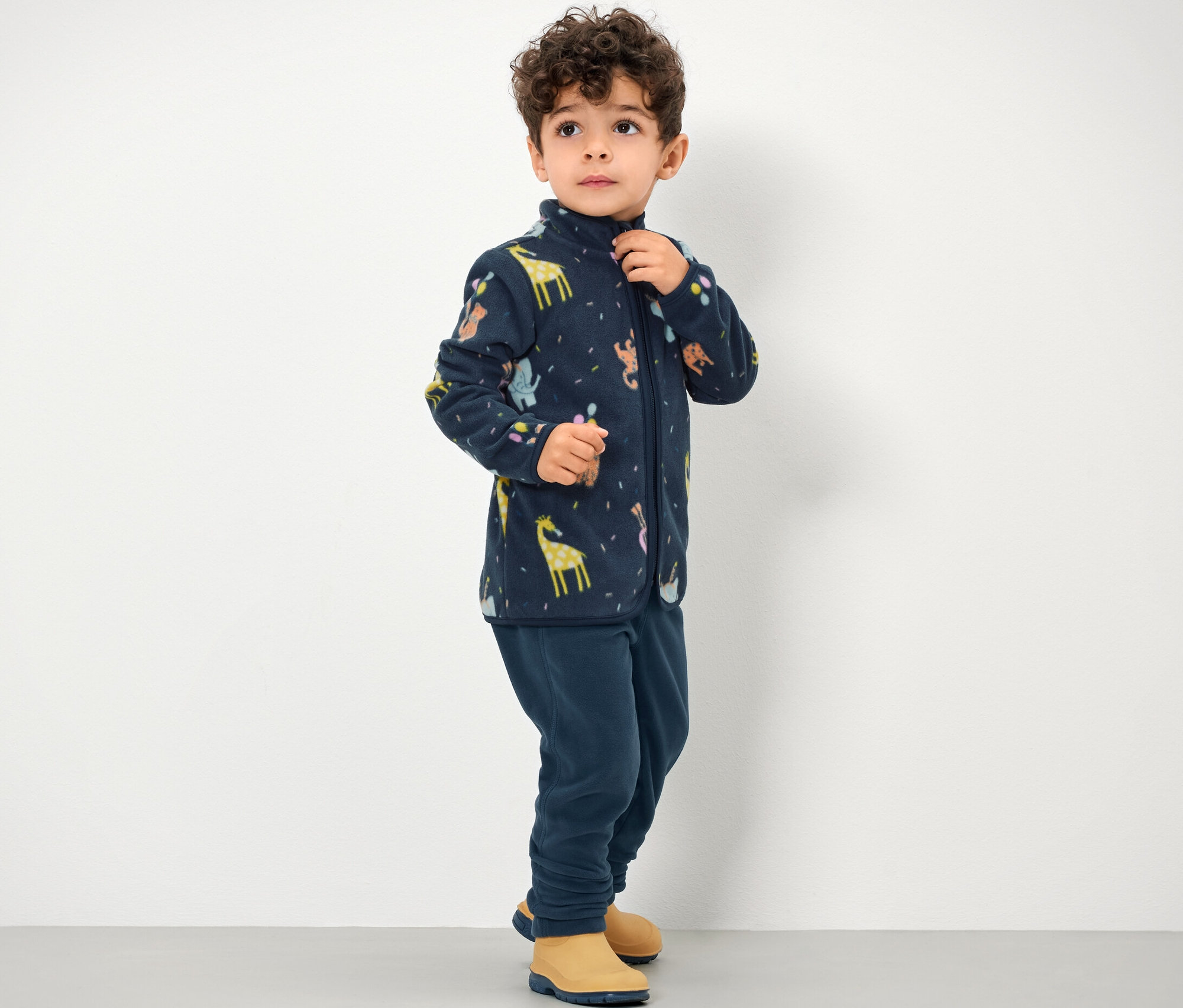 Chłopiec ma na sobie spodnie polarowe i bluzę rozpinaną na zamek z nadrukiem zwierzęcym.