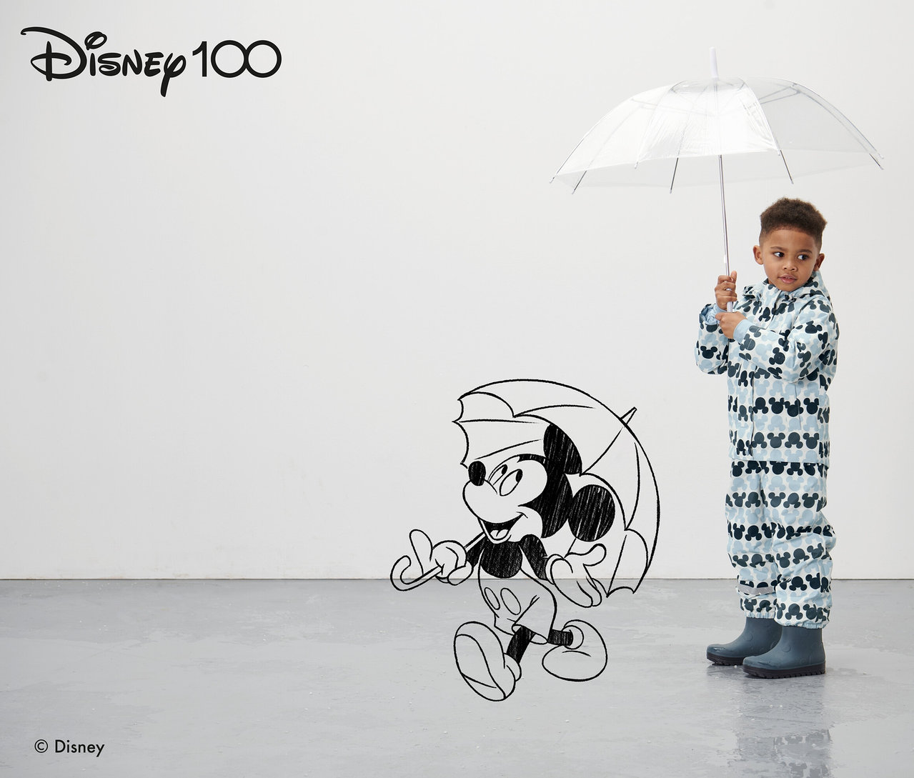 Chłopiec trzyma przezroczysty parasol. Ma na sobie niebieską dziecięcą kurtkę przeciwdeszczową »Micky«.