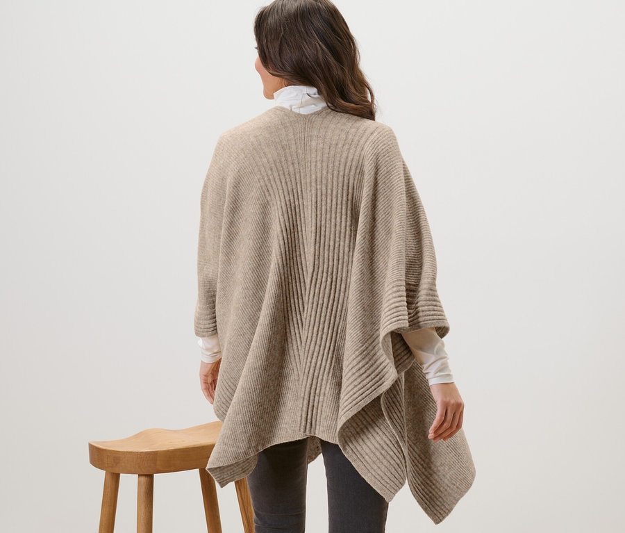 Kobieta stoi tyłem, ubrana w ponczo z dzianiny.