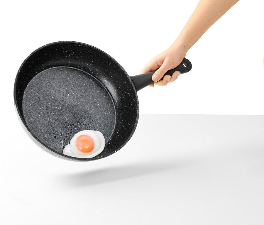 Ręka trzyma 28 cm profesjonalną patelnię z imitacji granitu z jajkiem sadzonym.