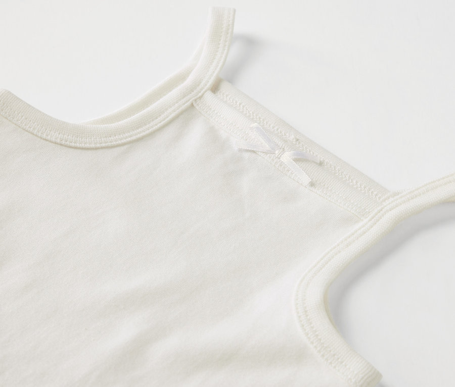 Zbliżenie na białe body niemowlęce na ramiączkach z kokardką.