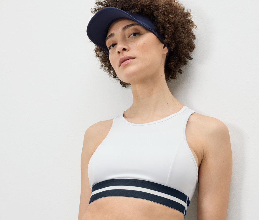 Kobieta ma na sobie białą sportową braletkę „Crop Top” i niebieski daszek.