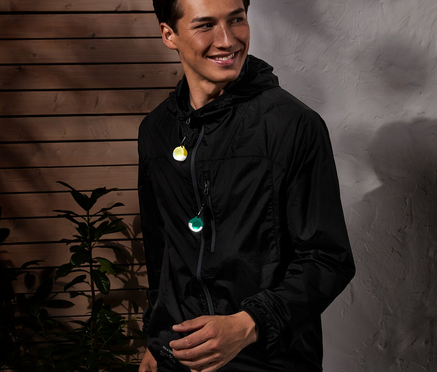 Mężczyzna w czarnej kurtce z kapturem z 3 sztukami przywieszek odblaskowych LED w kolorze żółtym i zielonym.