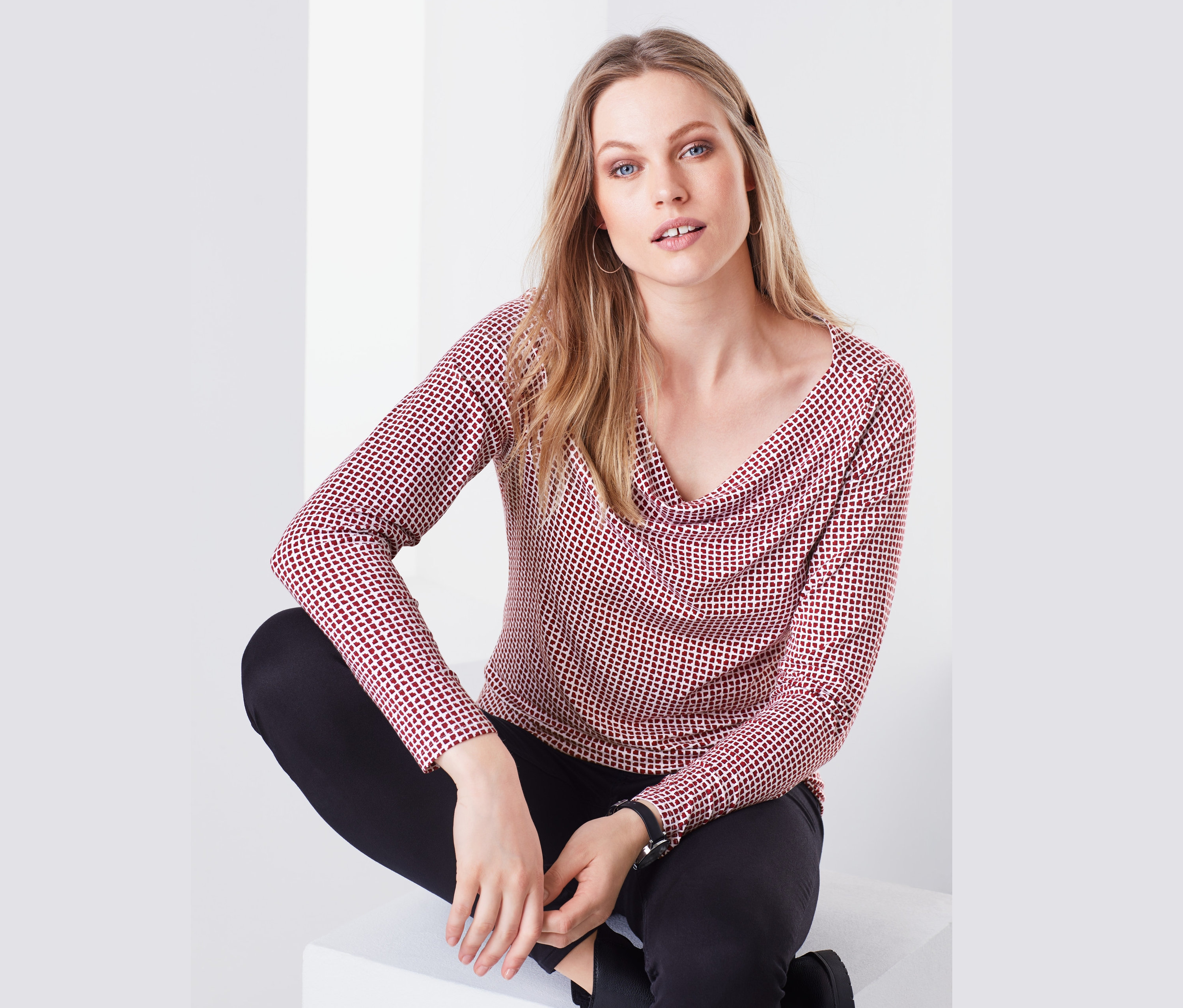 Kobieta siedzi i ma na sobie bluzkę z dekoltem typu woda.