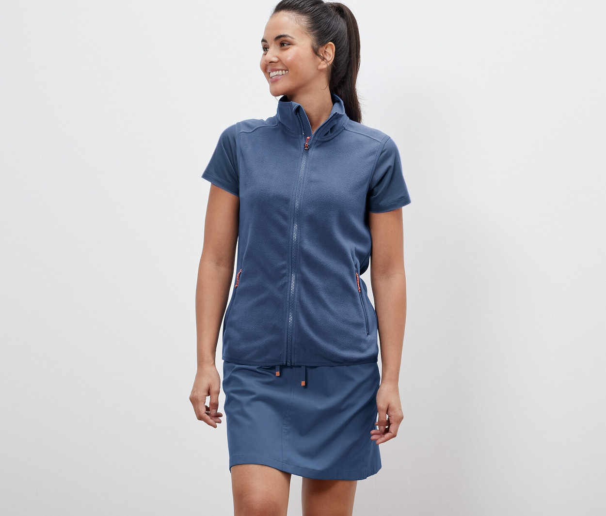 Kobieta ma na sobie kamizelkę polarową i spódnicę.