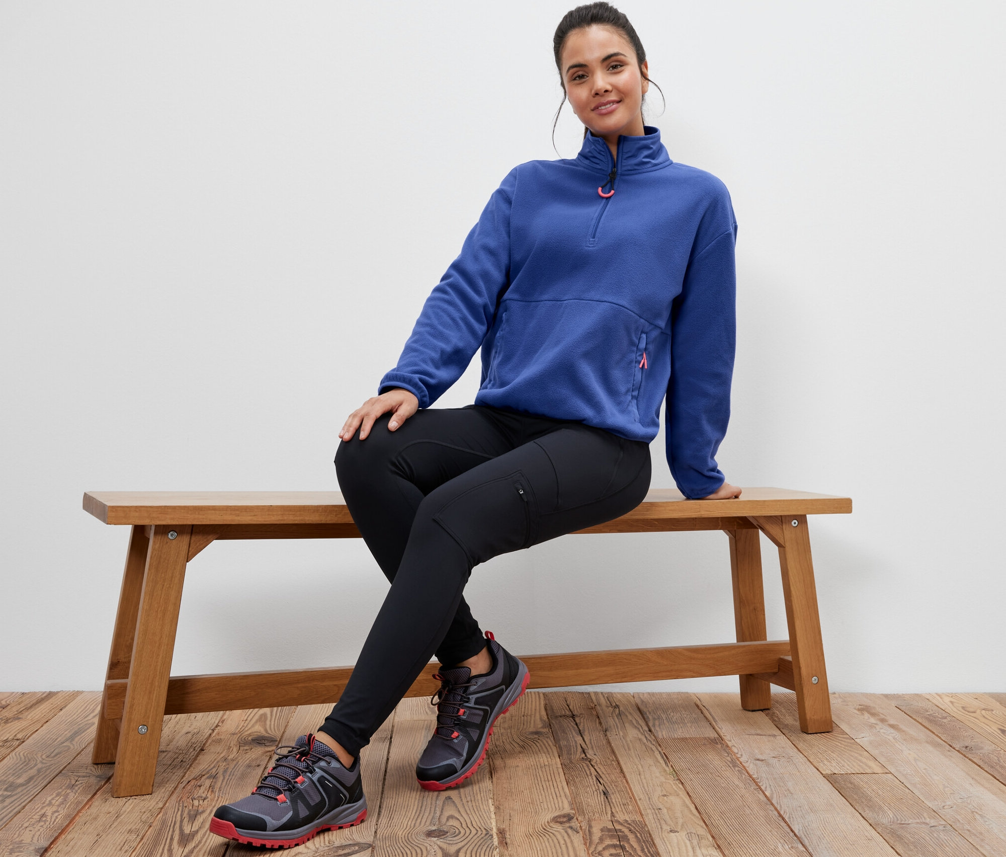 Kobieta siedzi na ławce, ubrana w bluzę z polaru w kolorze niebieskim.