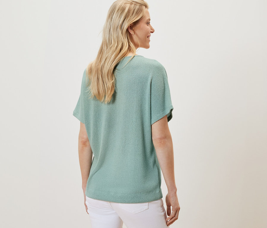 Widok z tyłu blondynki w szałwiowej koszulce z fakturowanej powierzchni i białych spodniach.