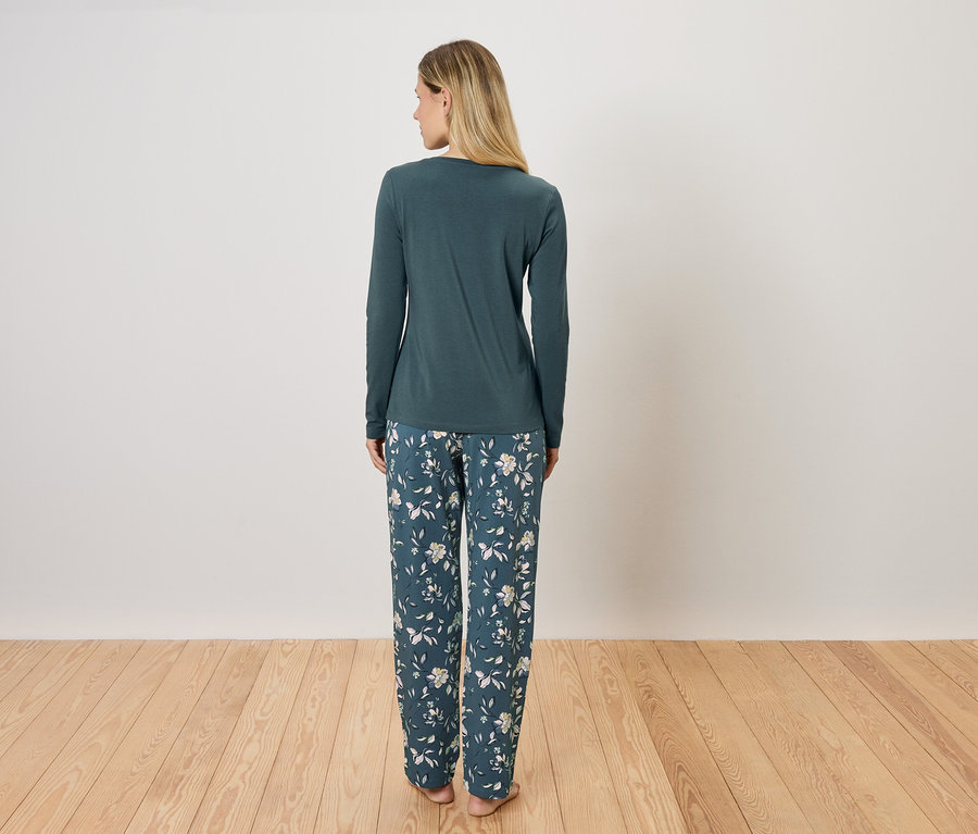 Kobieta stoi tyłem, ubrana w zieloną piżamę z długim rękawem i kwieciste spodnie.