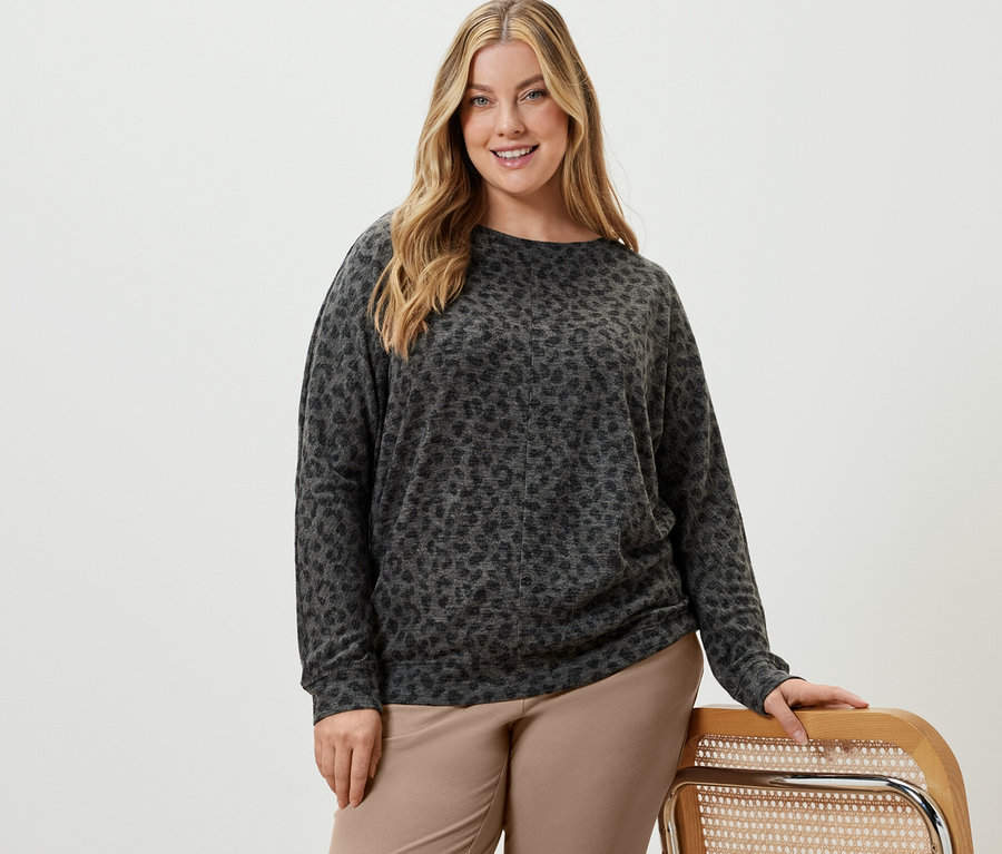 Kobieta pozuje w beżowych spodniach dresowych i wzorzystej bluzce z rękawami typu nietoperz.