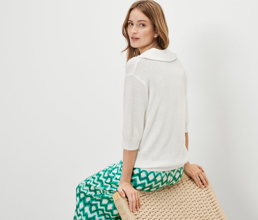 Kobieta siedzi na stołku i ma na sobie biały letni sweter z dzianiny.