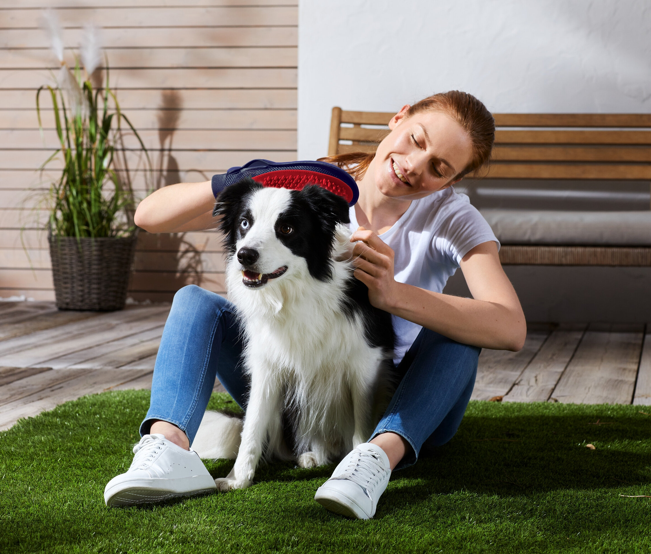 Kobieta siedzi na trawie i szczotkuje czarno-białego psa.