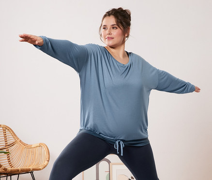 Kobieta w niebieskiej koszulce sportowej 2 w 1 i legginsach sportowych ćwiczy jogę na macie.