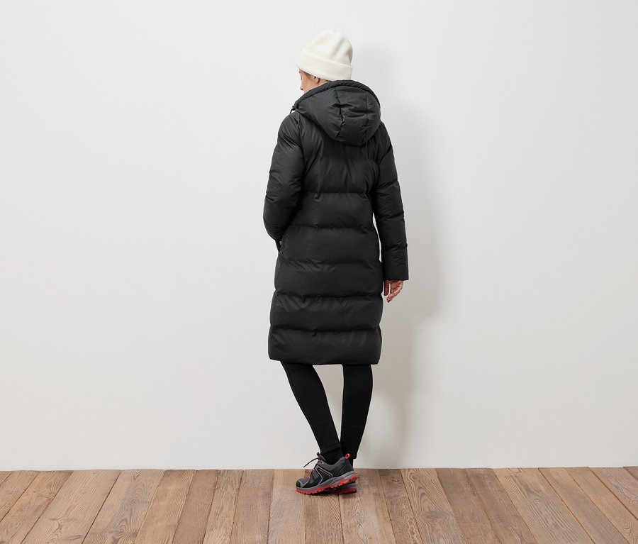 Kobieta tyłem do kamery ma na sobie czarną kurtkę puchową, czarne legginsy i białą czapkę.