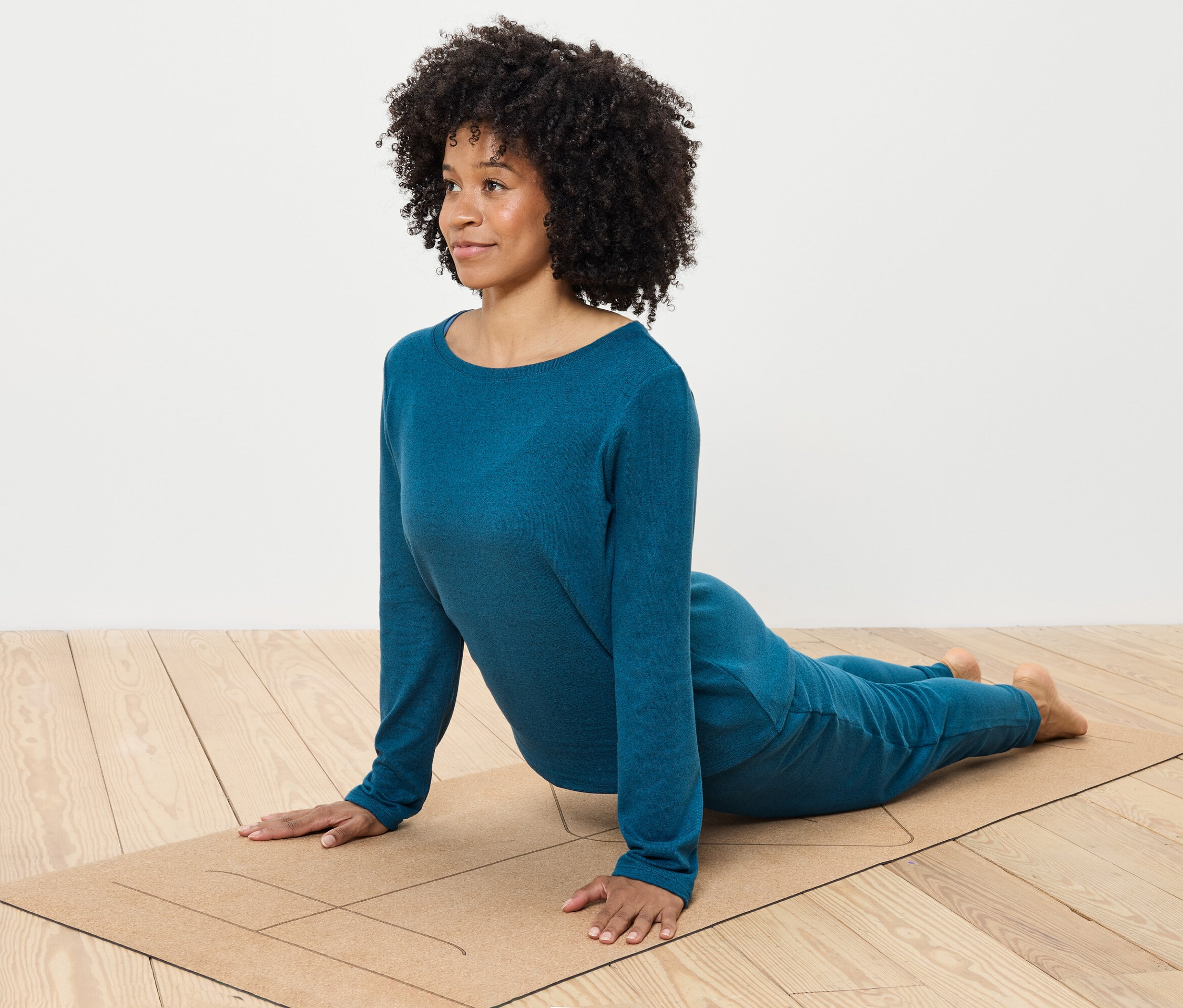 Kobieta z kręconymi włosami ćwiczy jogę w niebieskim ubraniu na macie.