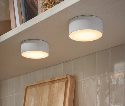 Dwie wielofunkcyjne lampy LED przymocowane do spodu półki. Na półce stoją słoiki z orzechami i książki.