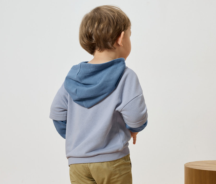 Widok z tyłu dziecka z blond włosami ubranego w niebiesko-szarą bluzę z kapturem i spodnie.