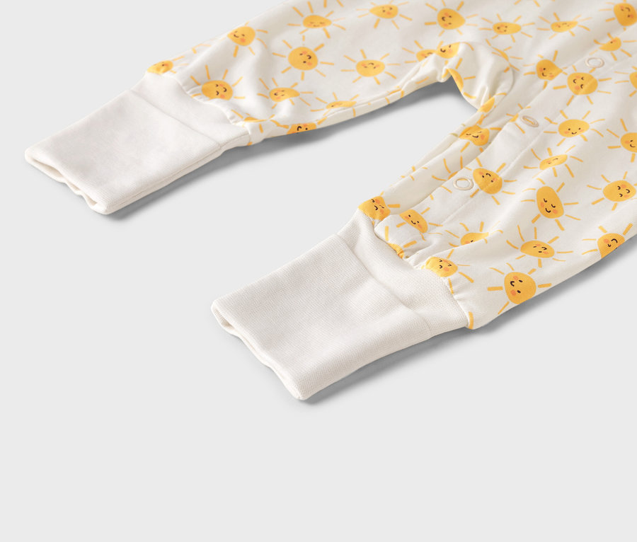 Zbliżenie na pajacyk niemowlęcy w żółte słoneczka z białymi mankietami.