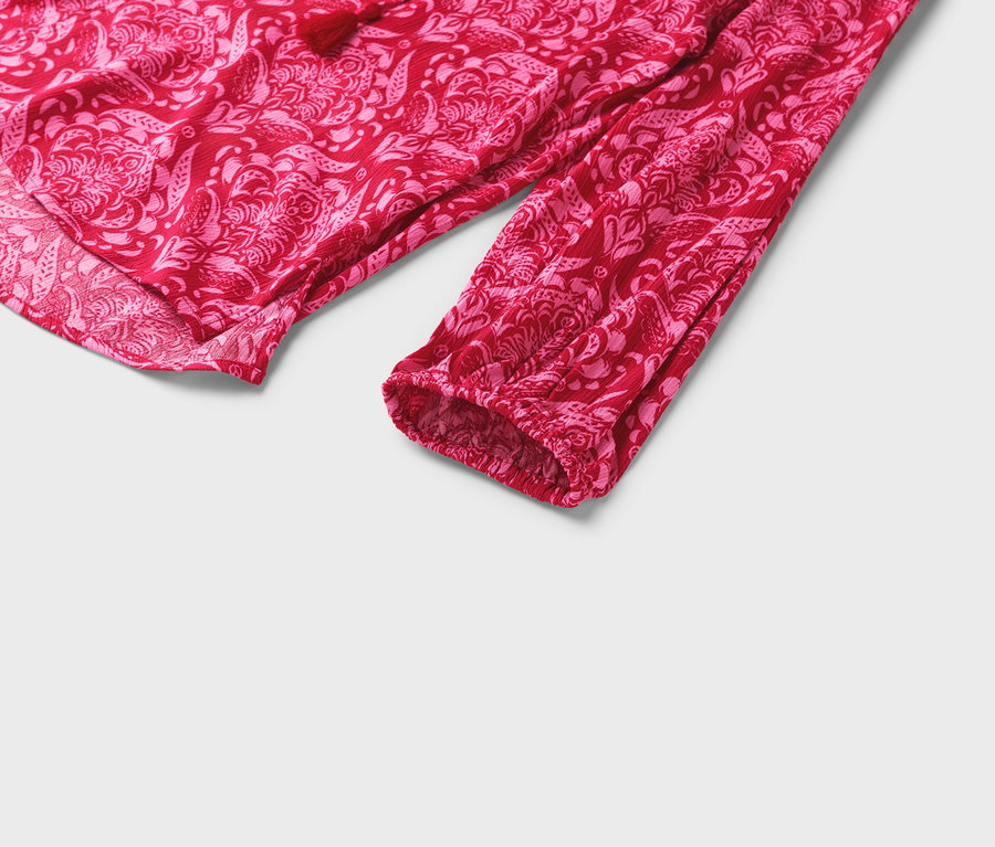 Zbliżenie na czerwoną bluzkę z różowym kwiatowym wzorem i długimi rękawami.