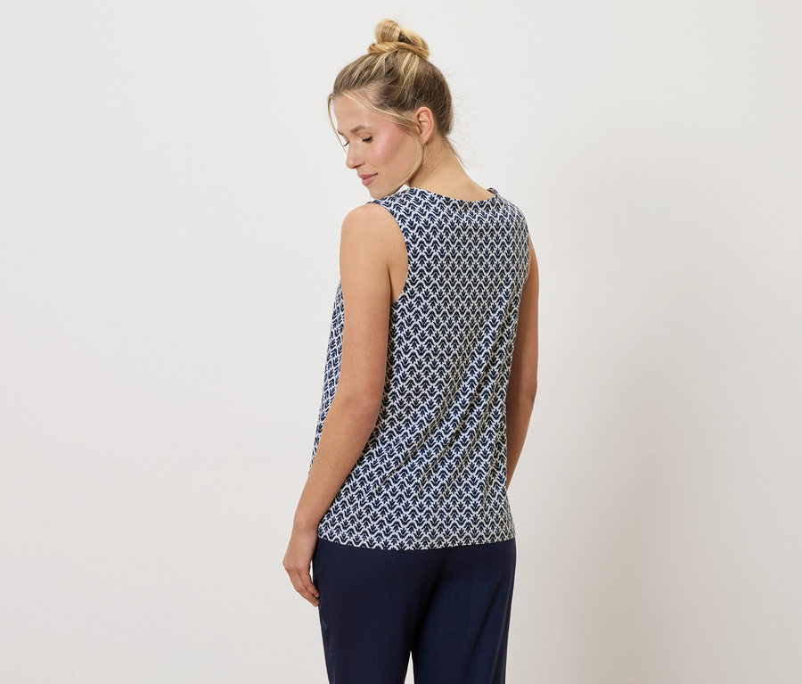 Blondwłosa kobieta z kokiem ubrana w granatowo-biały top bez rękawów i granatowe spodnie, widziana od tyłu.