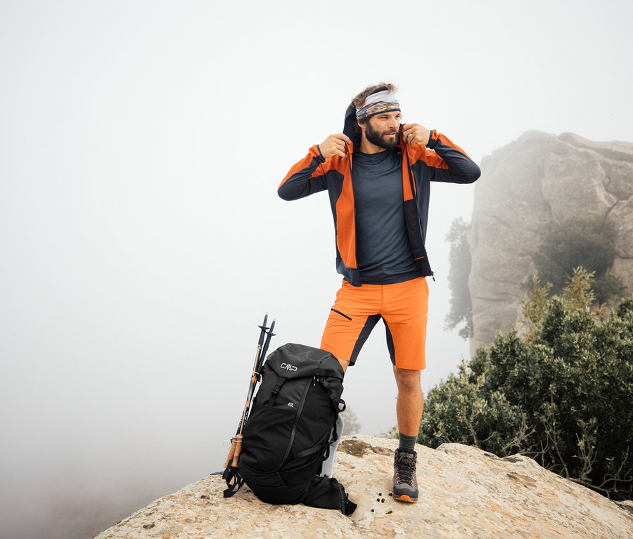 Mężczyzna stoi na skale z plecakiem trekkingowym CMP HAVRE, 40 litrów. Kijki trekkingowe oparte o plecak.
