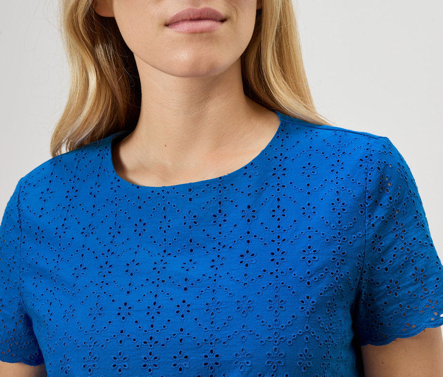 Zbliżenie kobiety ubranej w niebieską bluzkę z haftem angielskim.