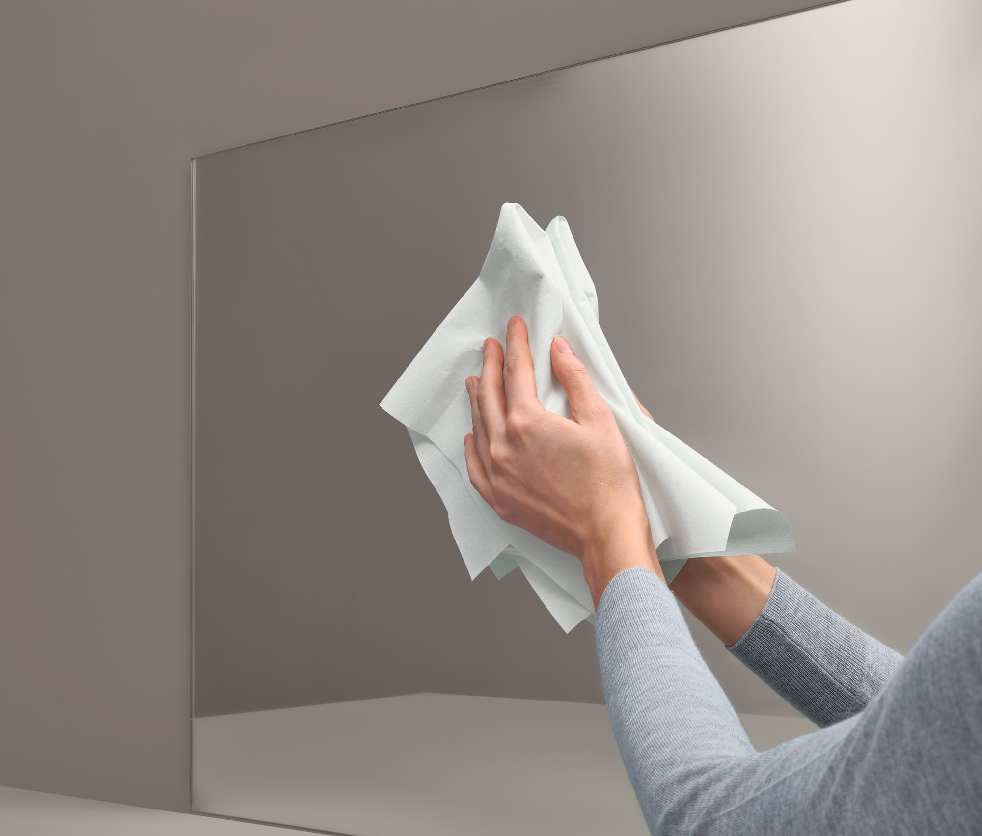 Kobieta czyści lustro Białą magiczną ściereczką do czyszczenia szyb i luster bez detergentów.