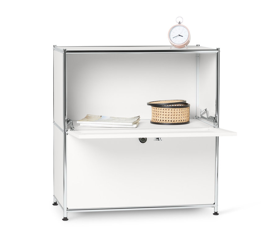 Biała metalowa szafka typu sideboard »CN3«, niska z komorami z klapami, na której leżą zegar, kosz i czasopisma.