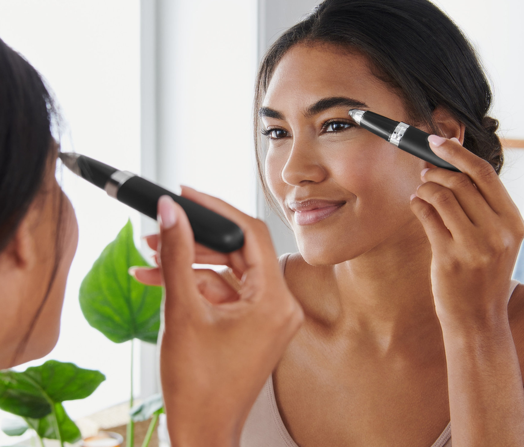 Kobieta stylizuje brwi elektrycznym trymerem do brwi przed lustrem.