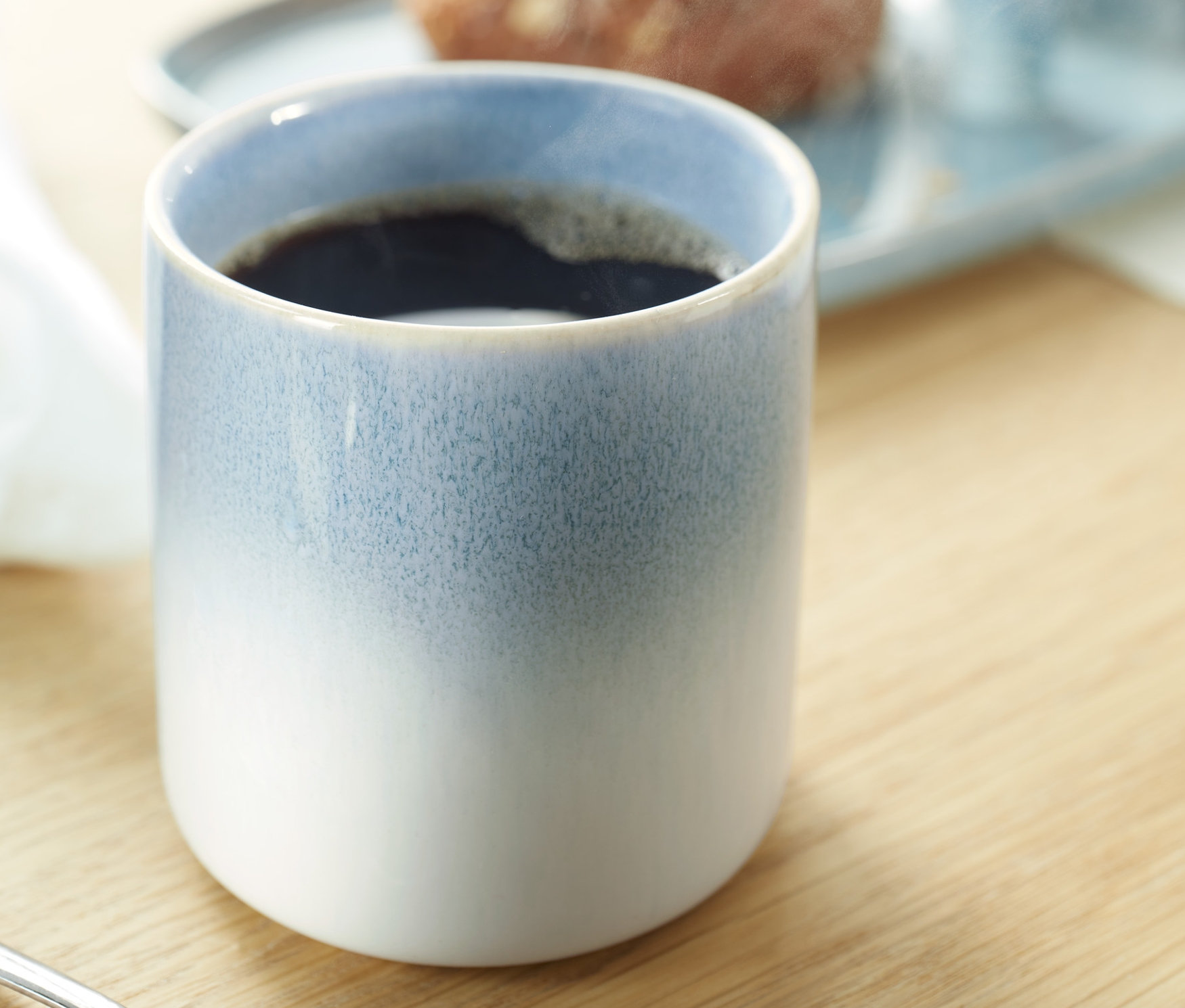 Zbliżenie na kubek do kawy. W tle widoczny talerz z jedzeniem.