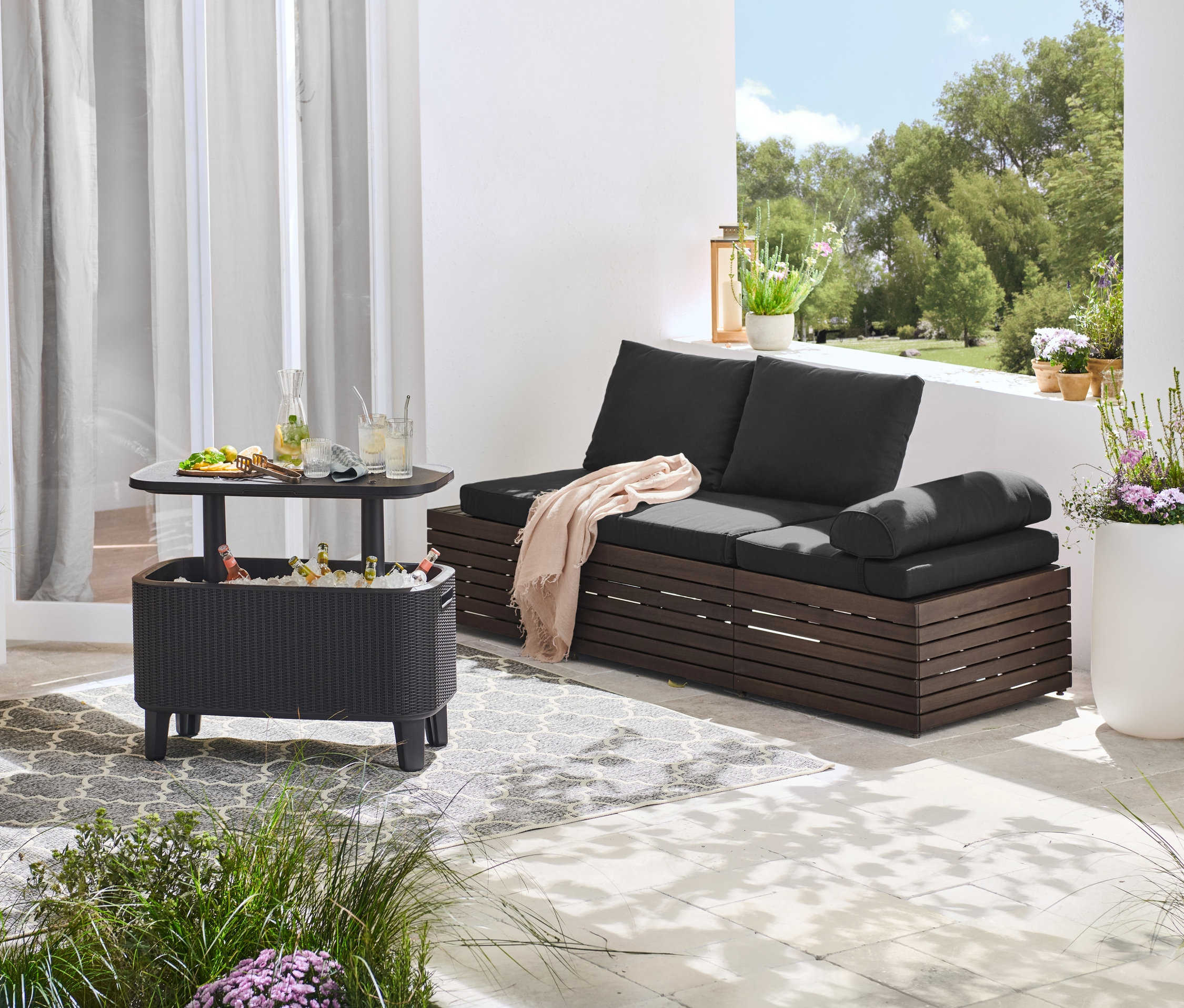 Czarna sofa 2 w 1 z poduszkami stoi obok barku chłodzącego z napojami i przekąskami.