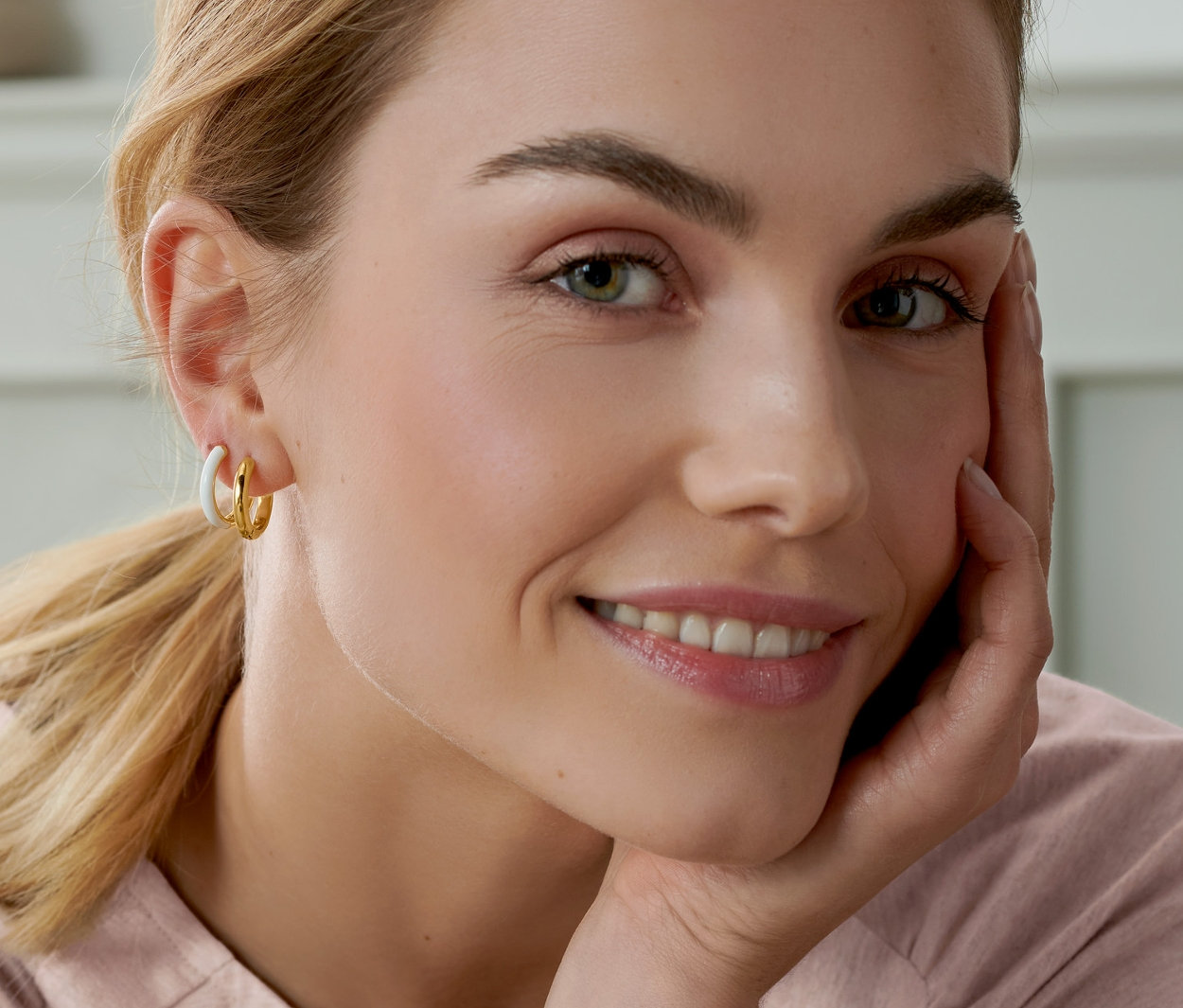 Uśmiechnięta kobieta opiera twarz na dłoni i ma na sobie kreole, 2-częściowy zestaw, pozłacane.