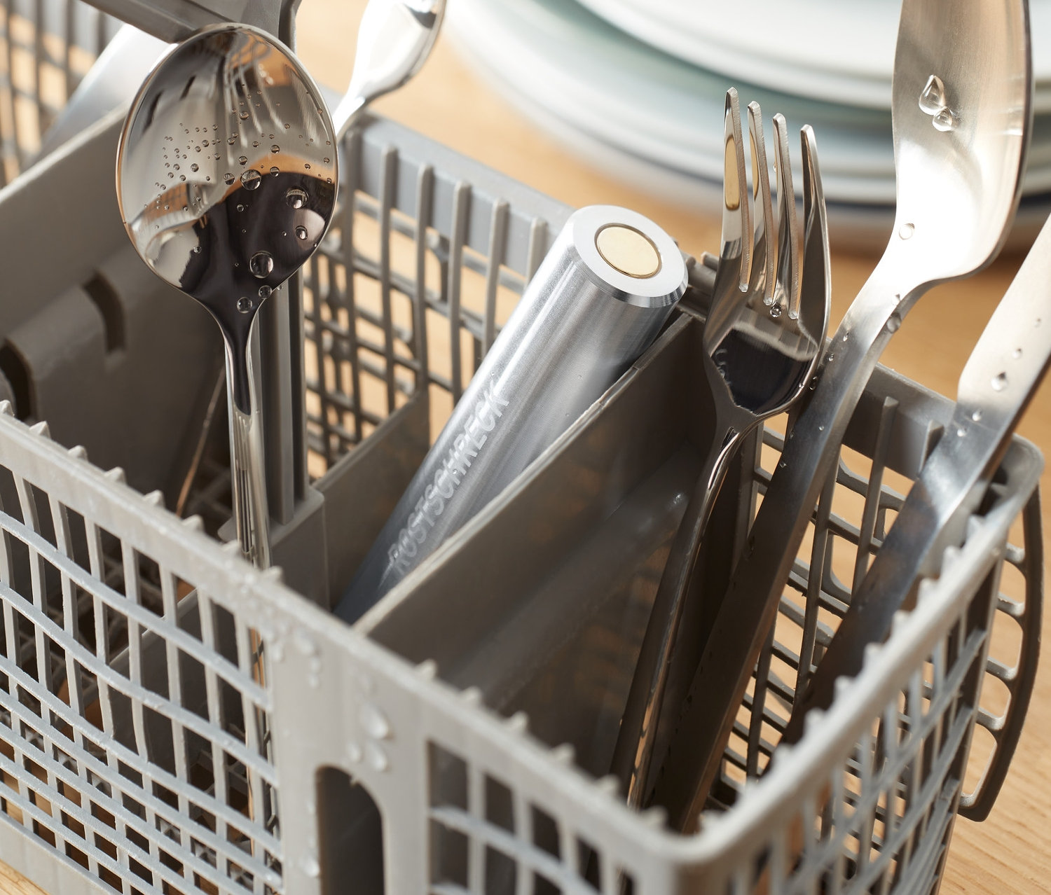 Srebrne sztućce w szarym koszyku w zmywarce z Odrdzewiaczem do zmywarki.