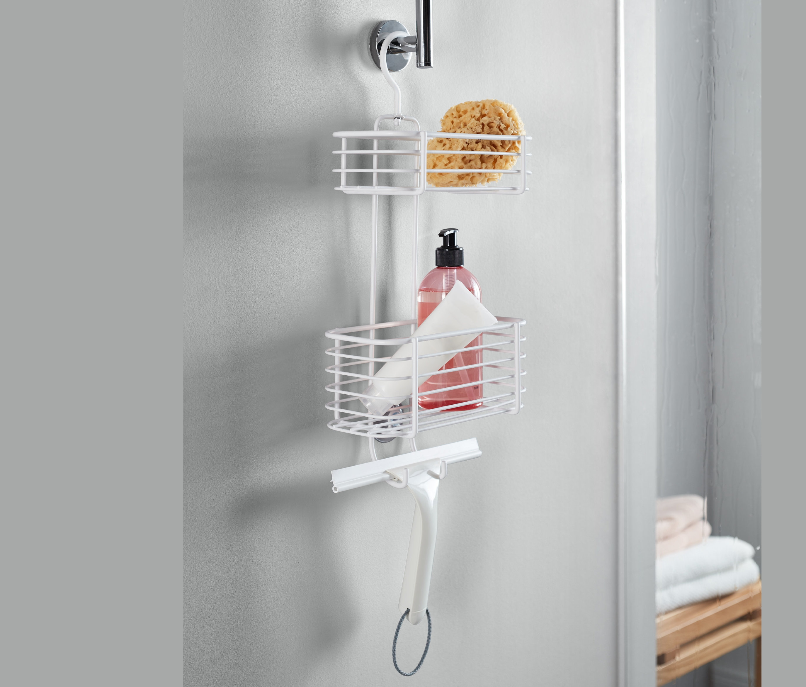 Biały wiszący regał pod prysznic z gąbką, butelką i ściągaczką.