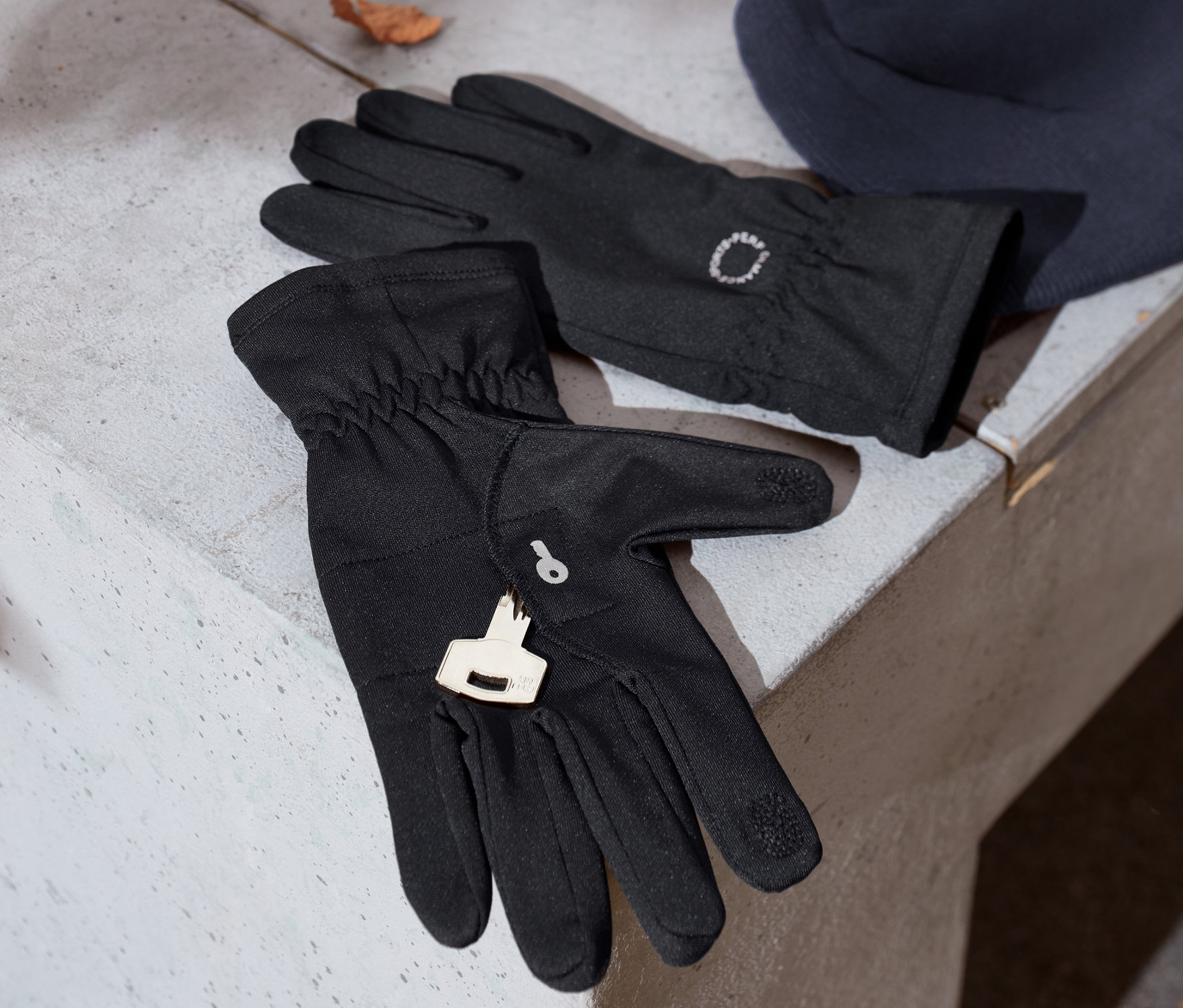 Czarne rękawiczki do biegania z odblaskowym nadrukiem leżą obok niebieskiej czapki z dzianiny na betonowej ławce.