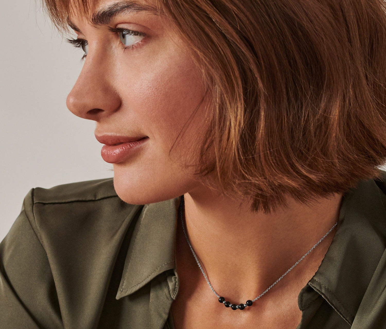 Profil kobiety z brązowymi włosami i zielonej koszuli, noszącej naszyjnik z obsydianu energetycznego.