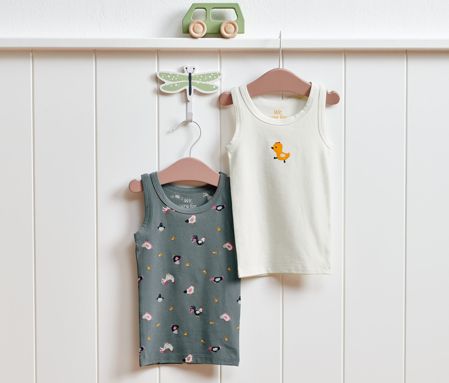 Dwie dziecięce podkoszulki z nadrukiem w gospodarstwo wiszą na wieszakach na białej ścianie.