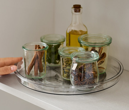 Dłoń sięga po obrotową paterę z przyprawami na półce.